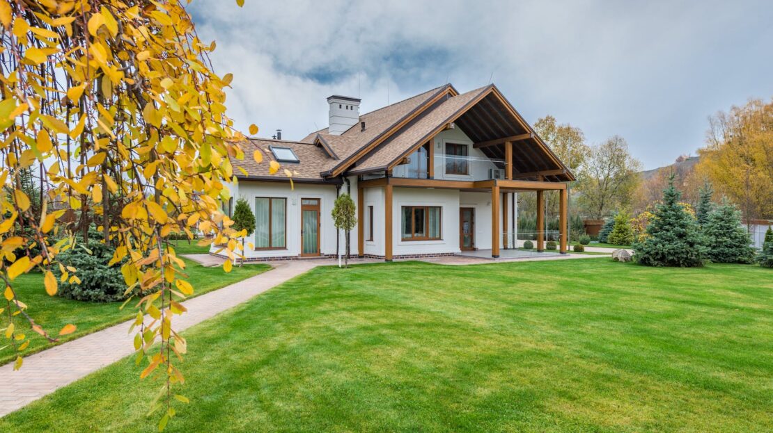 Exterior of residential suburban cottage with balcony surrounded with lush green plants and trees
